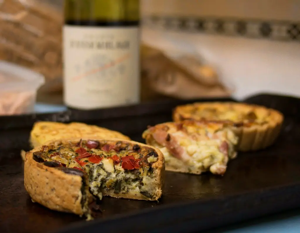 Handmade individual quiches with herbs, red pepper, and ham on a baking tray