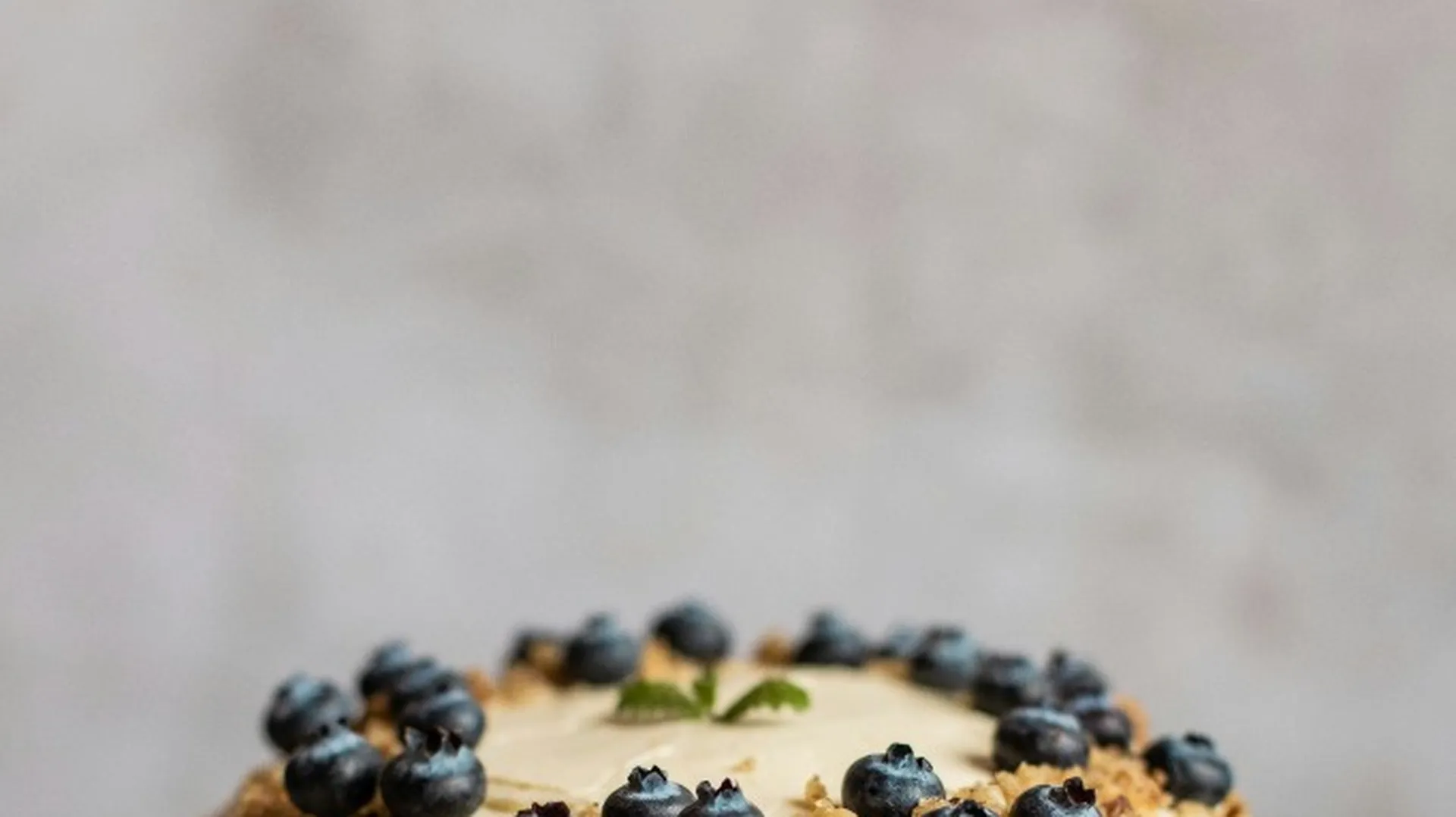 Homemade layer cake topped with cream frosting, blueberries, and chopped nuts